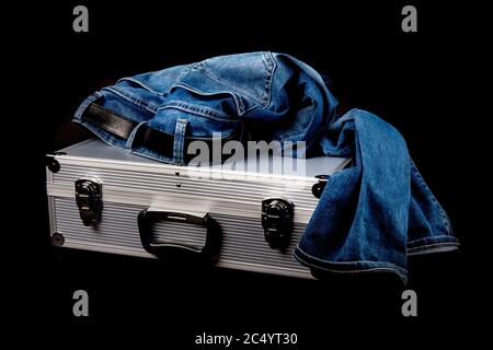 une paire de vieux jeans bleus reposant sur une valise en aluminium isolée sur le noir Banque D'Images