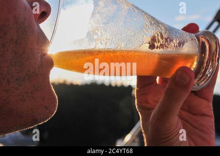 Gros plan sur un homme non rasé qui boit une bière à l'extérieur. Rétroéclairé par le soleil. Personnes, boissons, alcool, loisirs, concept de style de vie. Autorisation du modèle Banque D'Images