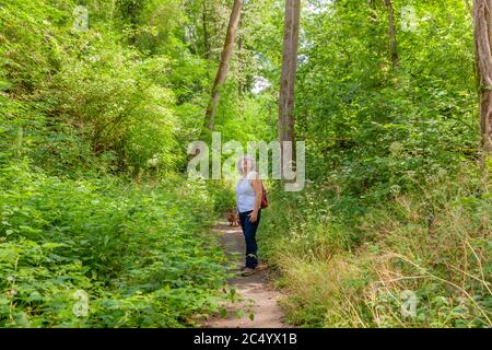 Femme mexicaine mûre avec son chien debout regardant sur une route de terre entourée d'arbres et de végétation verte au milieu de la forêt Banque D'Images