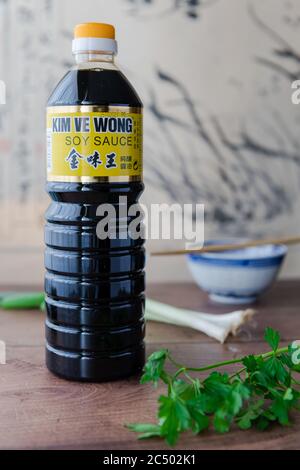 Une bouteille de sauce soja naturellement brassée de la marque Kim VE Wong sur un plan de cuisine avec du persil et des oignons de printemps. Banque D'Images