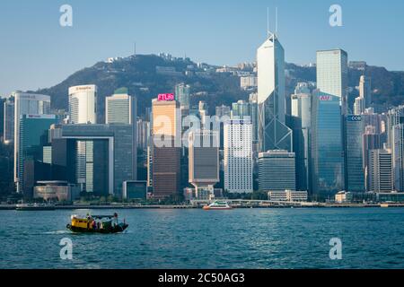 L'île de Hong Kong est en bord de mer avec ses gratte-ciel bondés et une jonque de voile traditionnelle passant par le port. Banque D'Images