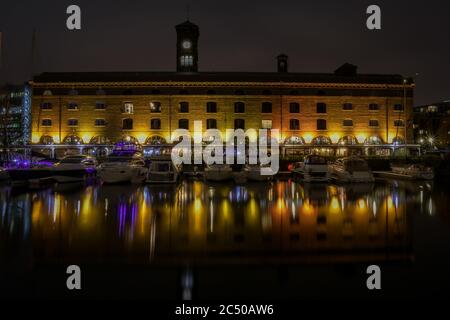 Vue nocturne de la marina de St. Katherine Dock à Londres avec le bâtiment et les bateaux de plaisance qui jettent un reflet sur l'eau fixe. Banque D'Images