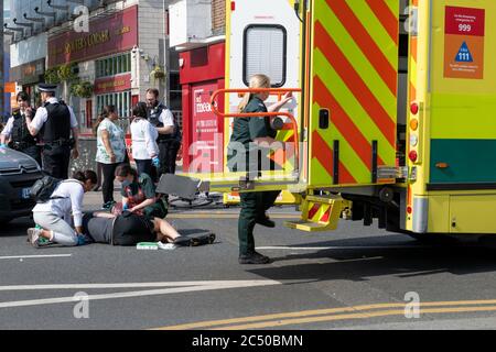 Un cycliste de livraison à domicile blessé dans un accident recevant des soins sur la route avec la police et l'ambulance d'urgence sur les lieux. Banque D'Images