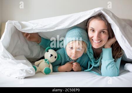 Bonne mère et enfant, garçon, avec une tenue assortie, allongé dans le lit, souriant heureux, embrassant et se cachant sous la couverture Banque D'Images