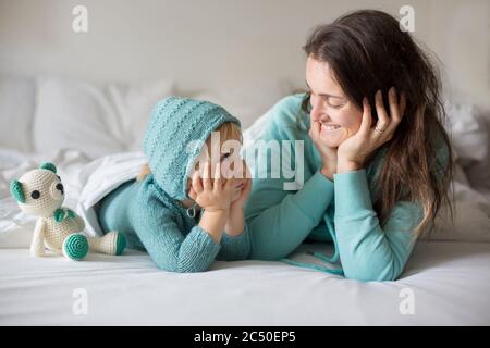 Bonne mère et enfant, garçon, avec une tenue assortie, allongé dans le lit, souriant heureux, embrassant et se cachant sous la couverture Banque D'Images