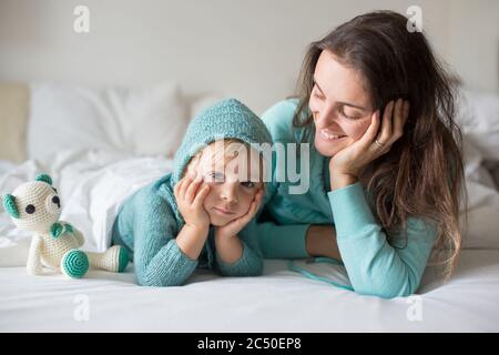 Bonne mère et enfant, garçon, avec une tenue assortie, allongé dans le lit, souriant heureux, embrassant et se cachant sous la couverture Banque D'Images