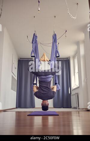 Un jeune homme pieds nus pendu à l'envers dans un studio de yoga Banque D'Images