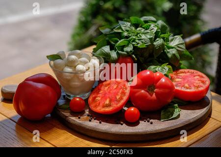 Ingrédients pour salade italienne traditionnelle caprese - tomate, bazil et mozzarella sur une assiette en bois. Tourné par une journée ensoleillée à l'extérieur Banque D'Images