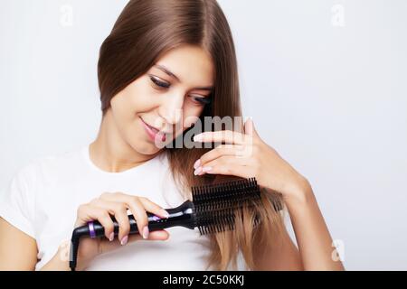 Jeune femme aux cheveux luxueux, il redresse avec un fer à friser Banque D'Images