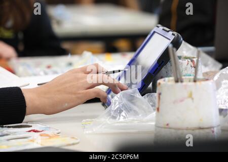 L'étudiant en art visuel moderne dans le studio de classe peint et utilisant une tablette numérique en ligne. Environnement pratique scolaire ou universitaire. Banque D'Images