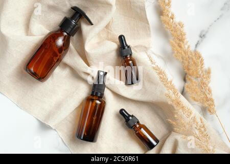Collection de bouteilles en verre ambré avec tissu beige et fleurs sèches sur fond de marbre. Cosmétiques naturels biologiques, maquettes d'emballage. Banque D'Images