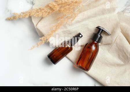Ensemble de bouteilles en verre ambré foncé avec tissu beige et fleurs sèches sur fond de marbre. Luxe produits beauté emballages mockups, concept de soins de la peau. Banque D'Images