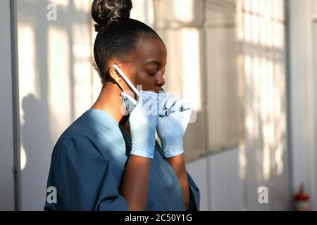 Une infirmière africaine fatiguée qui prend son masque facial ressent le stress à l'hôpital. Banque D'Images