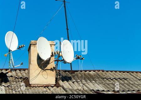 Plats satellites sur le vieux toit contre le ciel bleu Banque D'Images