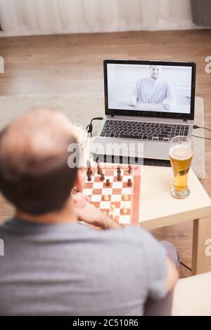 Des hommes intelligents jouant aux échecs sur appel vidéo pendant la quarantaine. Banque D'Images