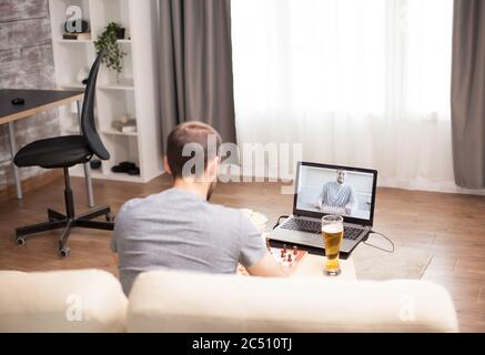 Homme assis sur un canapé jouant aux échecs avec un ami sur un appel vidéo pendant la quarantaine. Banque D'Images