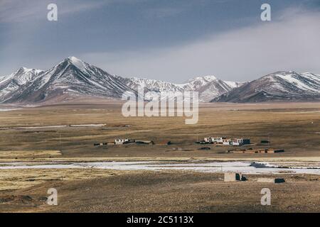 Un village tibétain sur la prairie, avec des montagnes enneigées dans le dos. Banque D'Images