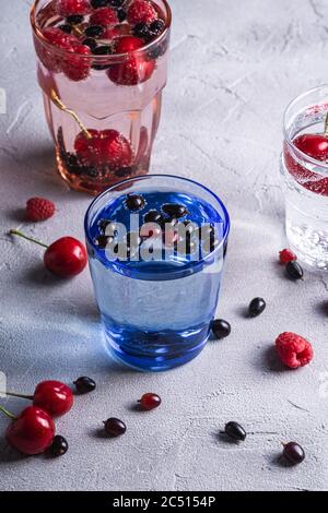 Eau fraîche et gazeuse buvez de cerise, framboise et cassis dans trois verres colorés sur fond de béton de pierre, boisson diététique d'été