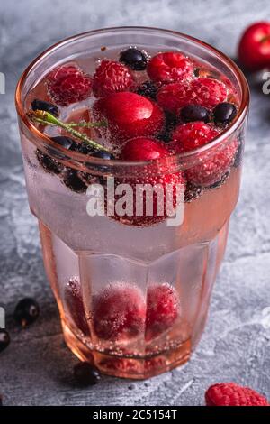 Eau fraîche et gazeuse buvez de cerise, framboise et baies de cassis en verre à facettes rouge sur fond de béton de pierre, boisson diététique d'été, un Banque D'Images