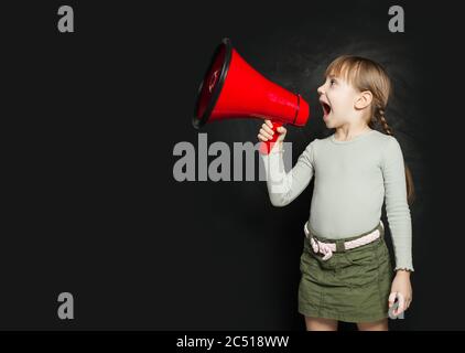 Petite fille drôle criant bruyamment à travers un mégaphone contre un tableau noir. Enfant avec haut-parleur Banque D'Images