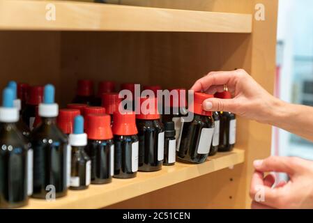 Une pharmacienne qui organise des flacons apothécaires en verre brun normé avec des bouchons et des gouttes scellés sur une étagère Banque D'Images