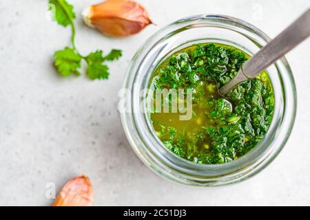 Sauce chimichurri traditionnelle fraîche pour la viande grillée dans un pot en verre, fond clair. Banque D'Images