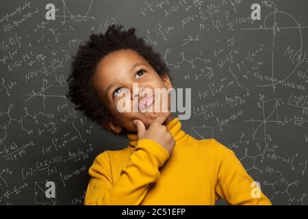 Enfant noir intelligent pensant sur fond de tableau noir avec des formules scientifiques Banque D'Images