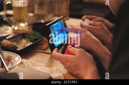 Deux hommes tenant des contrôleurs et jouant un jeu sur un Nintendo Switch installé sur une table dans un bar Banque D'Images