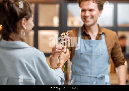 Portrait d'un vendeur gai en uniforme vendant de la crème glacée pour une jeune femme cliente à la boutique Banque D'Images