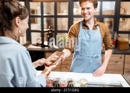 Portrait d'un vendeur gai en uniforme vendant de la crème glacée pour une jeune femme cliente à la boutique Banque D'Images