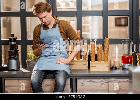 Le propriétaire d'affaires parle au téléphone tout en étant assis dans la petite boutique ou le café Banque D'Images