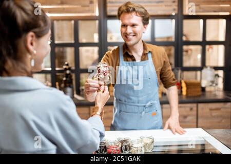 Portrait d'un vendeur gai en uniforme vendant de la crème glacée pour une jeune femme cliente à la boutique Banque D'Images