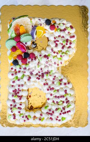 B lettre gâteau d'anniversaire avec bonbons aux fruits et biscuits au citron vert sur la surface dorée. Prêt pour la fête. Banque D'Images