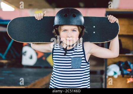 Un garçon de skate posé dans un casque dans un parc de skate. Garçon avec skateboard. Concept d'enfance, de lixiviation, de style de vie. Portrait enfant lad élégant avec skate Banque D'Images