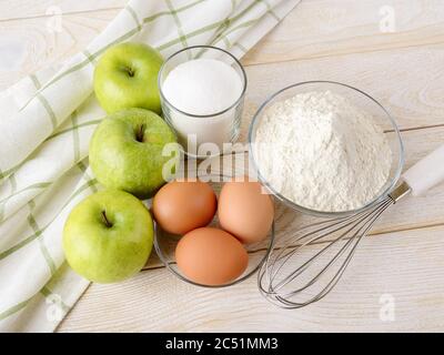 Ingrédients crus préparés pour cuire la tarte aux pommes : pommes vertes aigre, farine de blé, sucre et œufs sur une table en bois blanc. Recette facile pour un délicieux petit---petit-enfant fait maison Banque D'Images