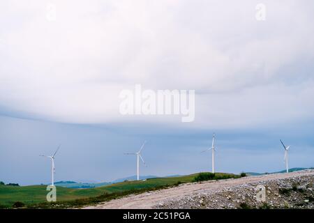 Quatre grandes éoliennes se trouvent en ligne sur la ligne d'horizon, contre les nuages de pluie bleus. Banque D'Images