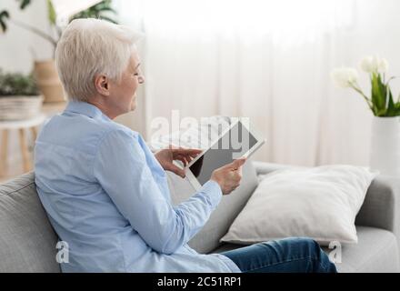 Technologies modernes pour les aînés. La vieille dame lisant sur une tablette numérique à la maison Banque D'Images