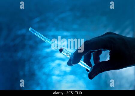 seringue pour la vaccination dans la silhouette de main sur fond bleu, gros plan sur un thème médical dans des couleurs sombres. Banque D'Images