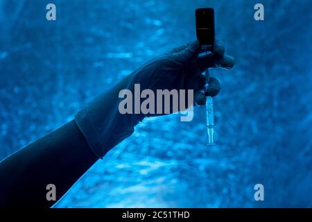 seringue avec flacon en verre pour la vaccination à la main dans la silhouette de gant médical sur fond bleu, gros plan sur un thème médical dans le col foncé Banque D'Images