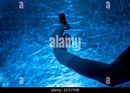 seringue avec flacon en verre pour la vaccination à la main dans la silhouette de gant médical sur fond bleu, gros plan sur un thème médical dans le col foncé Banque D'Images