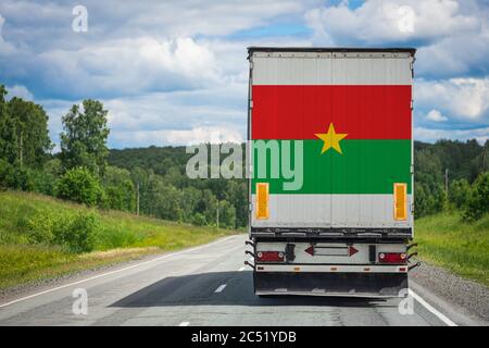 Un camion avec le drapeau national du Burkina Faso représenté sur la porte arrière transporte des marchandises vers un autre pays le long de la route. Concept d'exportation-impor Banque D'Images