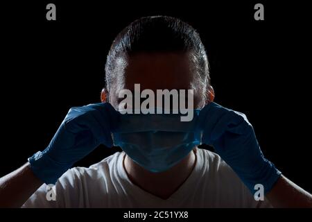 silhouette homme portrait d'un médecin mettant sur un visage un masque médical avec les mains dans des gants styry, gros plan d'un travailleur médical en contre-jour isolé sur Banque D'Images