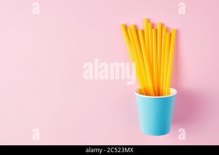 Pailles jaunes dans une tasse en papier bleu sur fond rose avec espace de copie. Vue sur une surface plane ou sur le dessus Banque D'Images