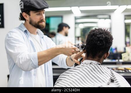 Vue latérale de l'homme avec une coupe de cheveux moderne et élégante, en regardant vers l'avant dans le salon de coiffure. Main de barber gardant le rasoir et coupant les cheveux sur la tête du client. Concept Banque D'Images