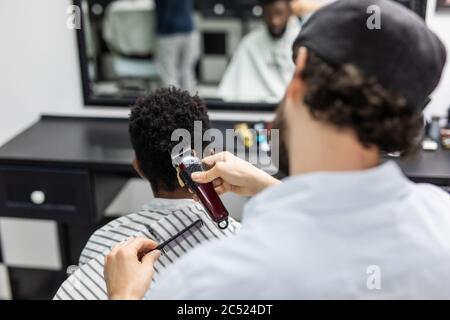 Vue latérale de l'homme avec une coupe de cheveux moderne et élégante, en regardant vers l'avant dans le salon de coiffure. Main de barber gardant le rasoir et coupant les cheveux sur la tête du client. Concept Banque D'Images