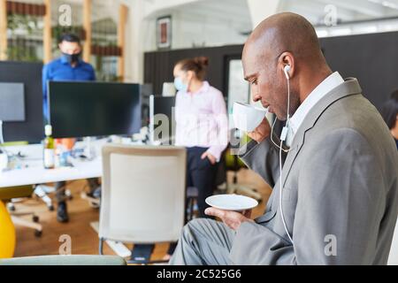 Homme d'affaires africain avec écouteurs intra-auriculaires et tasse à café dans un bureau ouvert Banque D'Images