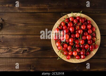 Cerises rouges sucrées dans un bol en bois sur une table en bois marron avec espace pour le texte. Vue de dessus. Banque D'Images