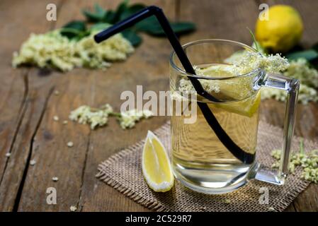 Un verre de jus de sureau naturel fait maison avec des fleurs de citron et de vieux sur une table en bois. Banque D'Images