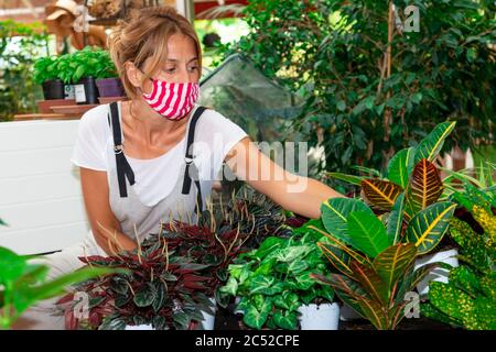 femme avec masque travaille dans une pépinière - femme avec masque avec un pot de fleur dans sa main Banque D'Images
