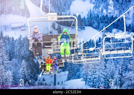 Garçon et fille s'assoient sur le télésiège avec des amis qui vont sur la deuxième chaise tous les enfants dans une tenue colorée sur la forêt de neige sur fond Banque D'Images